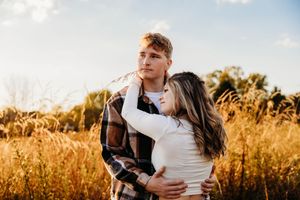A romantic couple embraces in a golden field at sunset creating a warm and intimate outdoor portrait.
