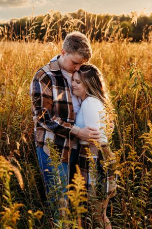 A couple embraces in a golden field of tall grass during sunset, with warm autumn lighting creating a romantic atmosphere.