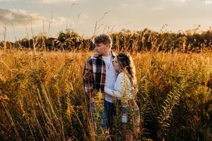 Romantic couple embraces in a golden wheat field at sunset creating a dreamy silhouette against the warm sky.