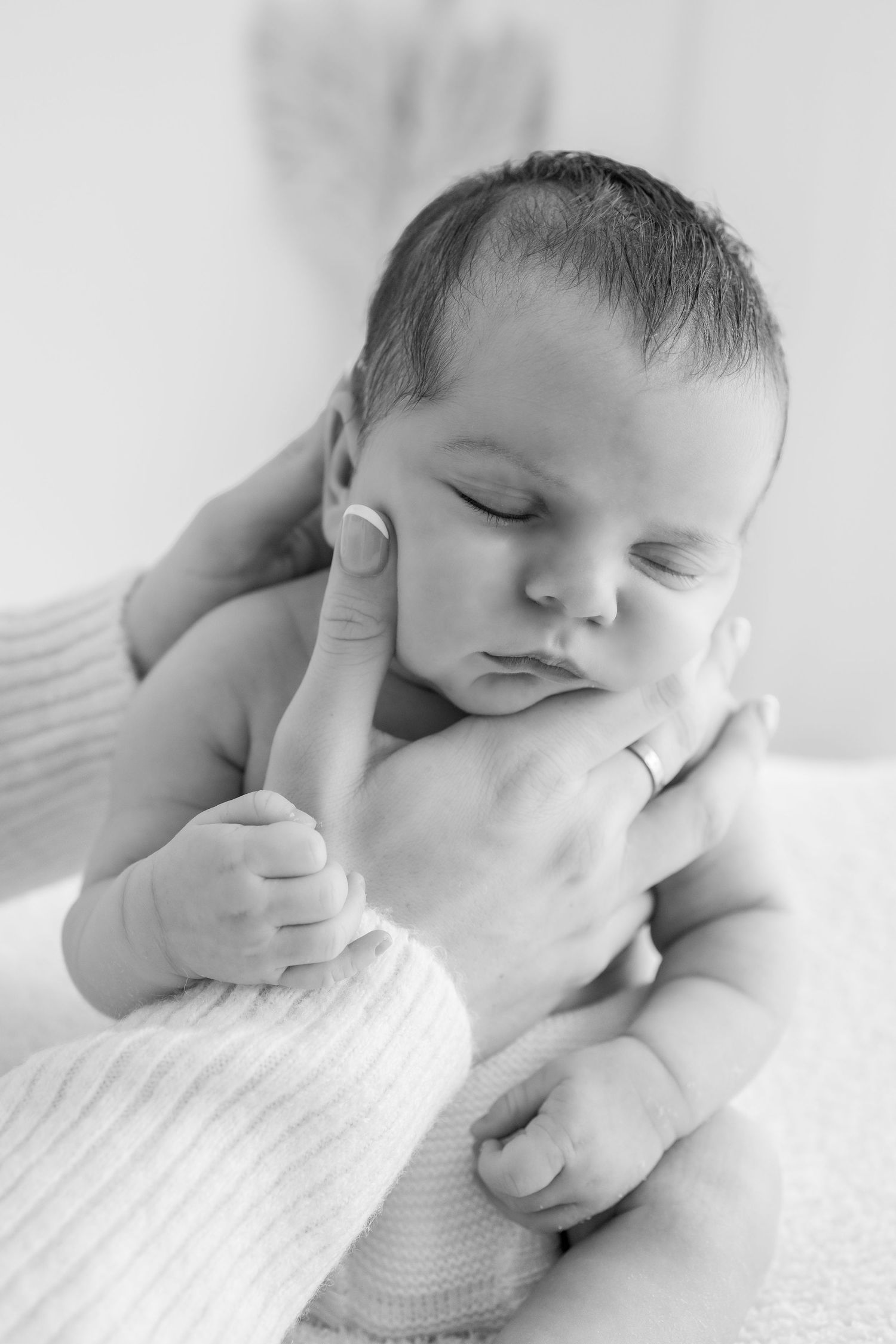 A series of black and white photos showing a sleeping baby in soft white bedding with their hand near their face.