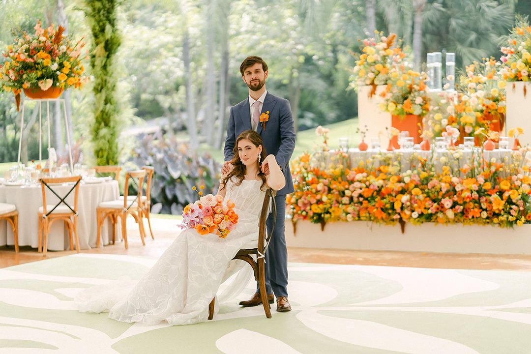 Elegant outdoor wedding reception with floral decorations in orange and peach tones on a garden terrace.