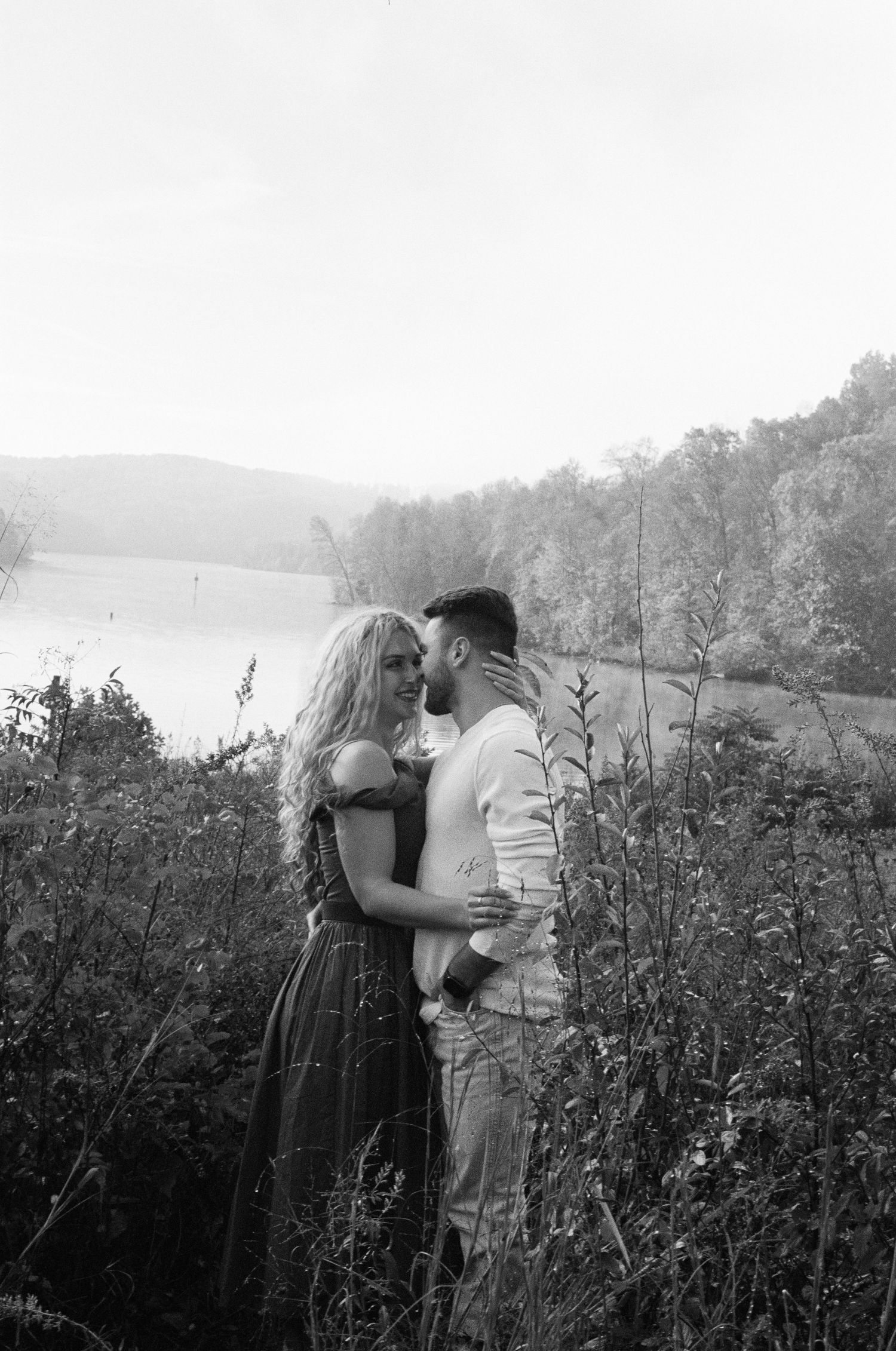 Romantic black and white portrait of a couple embracing by a lake.