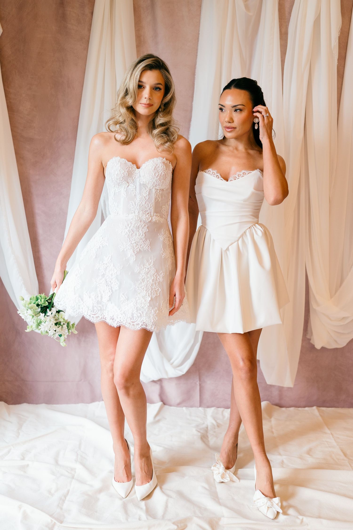 Models showcasing white bridal rompers against soft draped fabric backdrop.