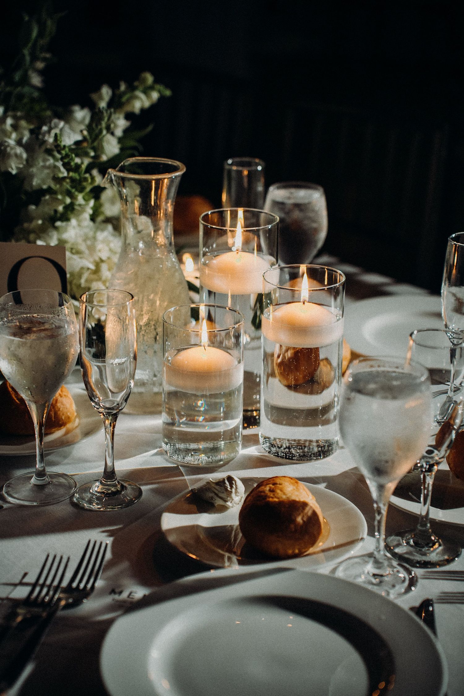 Elegant table setting with floating candles in glass holders, crystal stemware, and white plates for an upscale dinner event.