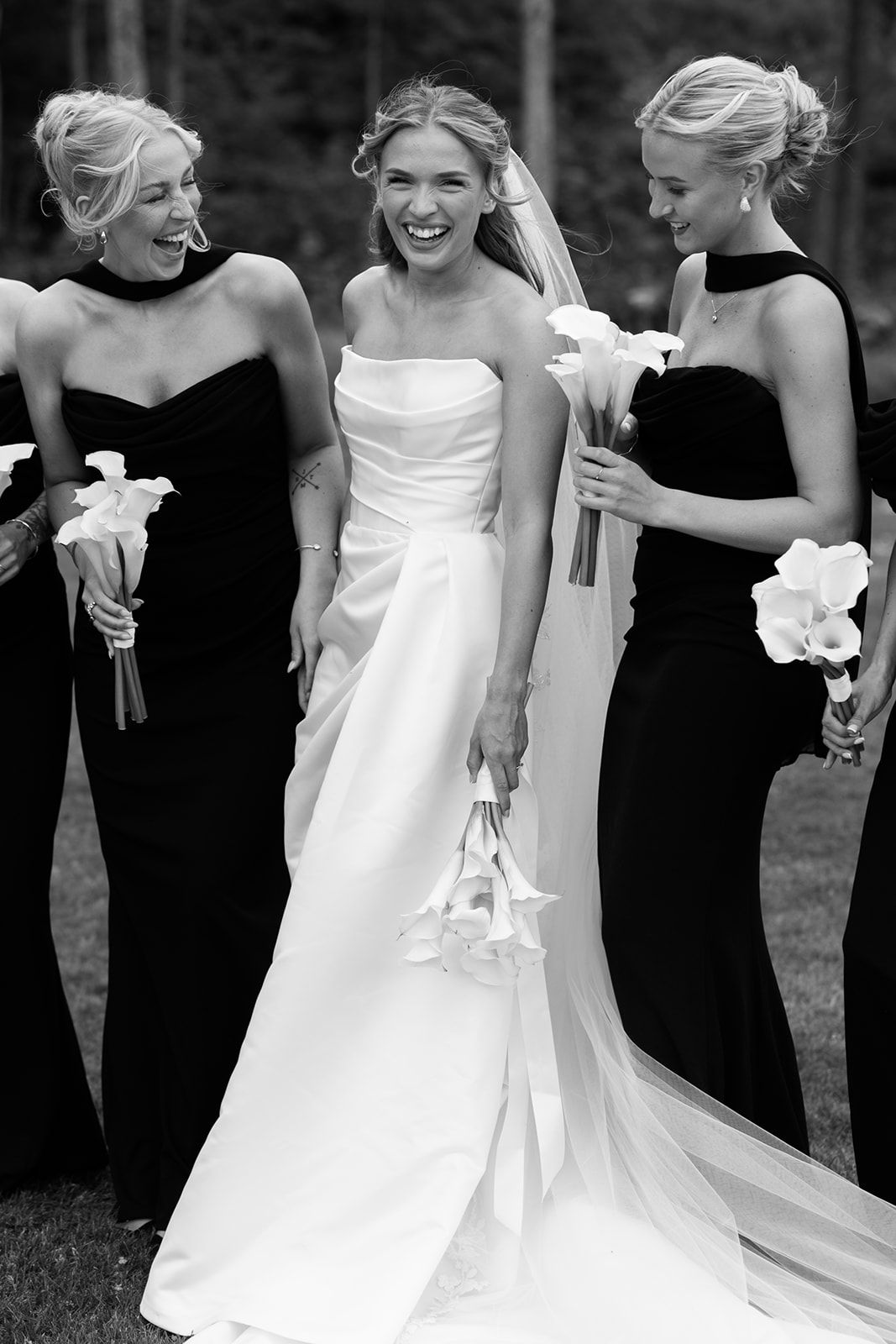 Bridesmaids in black dresses gather around bride in white gown during outdoor wedding celebration.