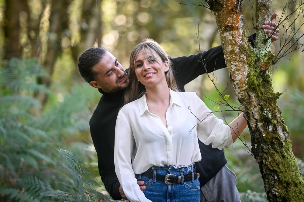 Couple in casual attire shares tender moments together in a lush forest setting during golden hour.