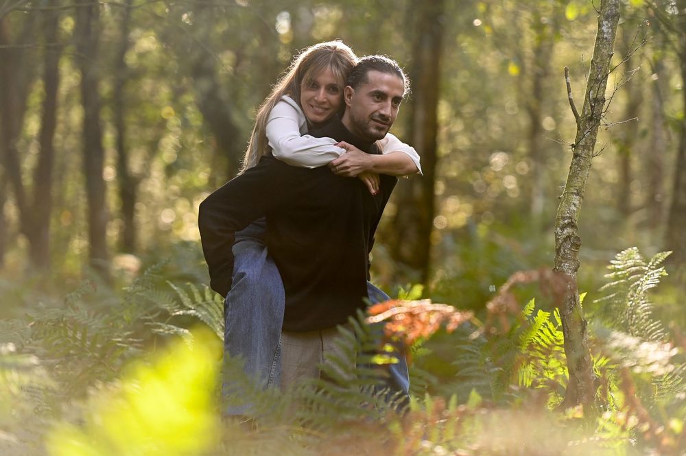 A couple embraces in a sunlit forest with soft bokeh effect and autumn foliage in the background.