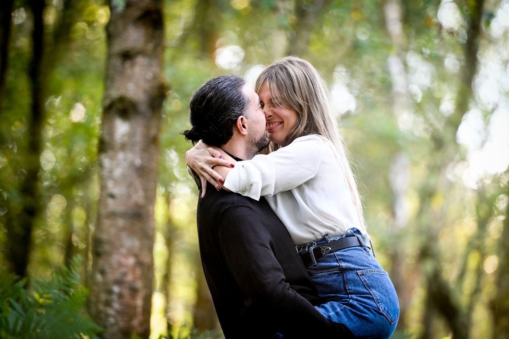 A romantic couple embraces in a sunlit forest setting during an outdoor photoshoot.
