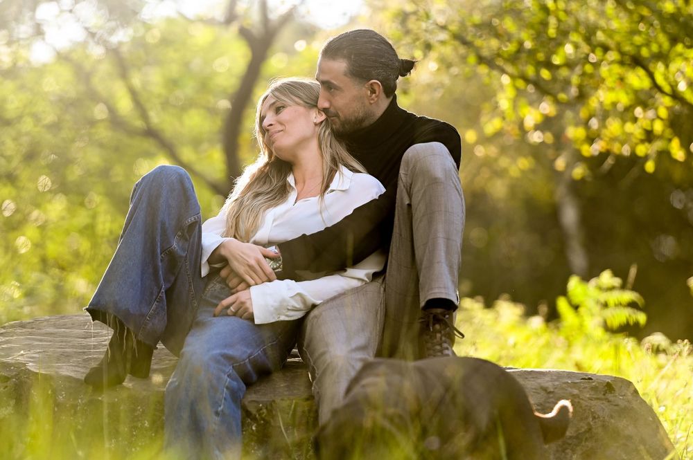 Couple embraces in a romantic moment outdoors during golden hour with autumn foliage in the background.
