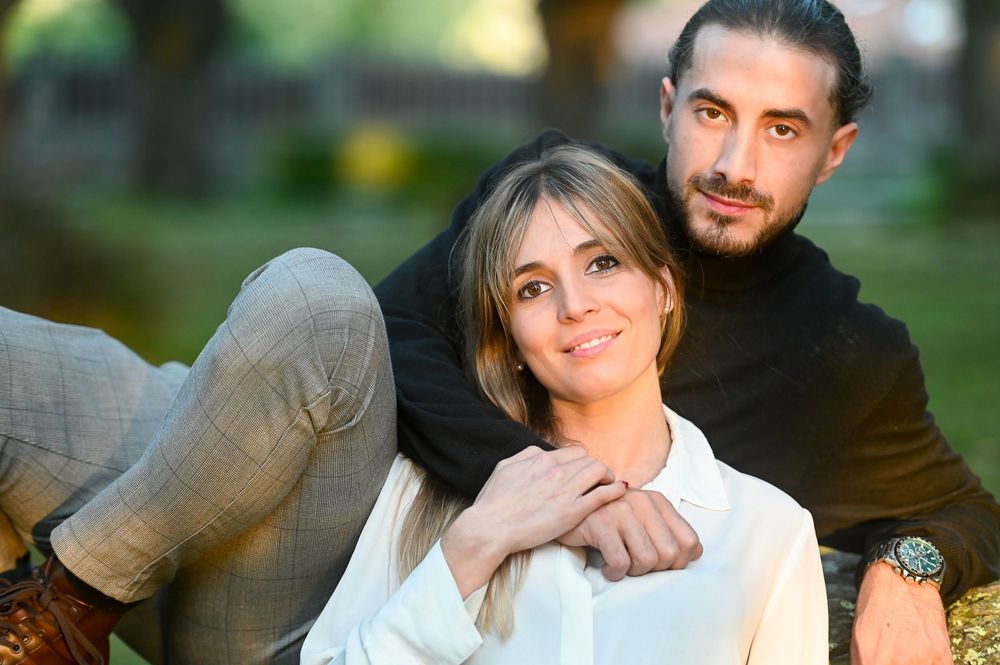 A couple sits together outdoors on grass, with soft natural lighting creating an intimate romantic portrait.
