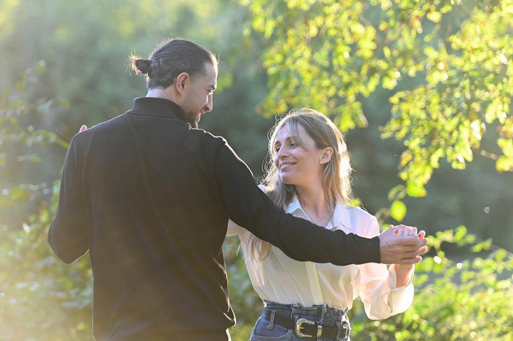 A couple dancing together in a sunny outdoor garden setting with backlit golden sunlight creating a romantic atmosphere.