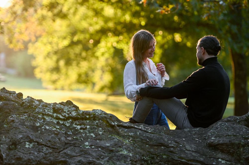 A couple sits together on large rocks during golden hour in a romantic outdoor setting.