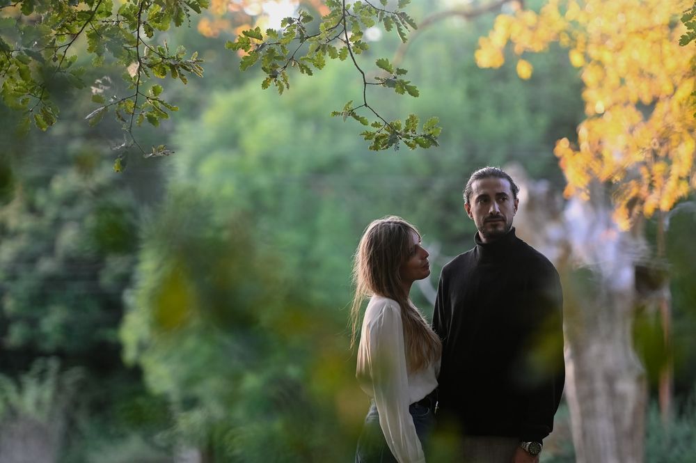 A couple shares a romantic moment surrounded by autumn foliage in a park setting during golden hour.