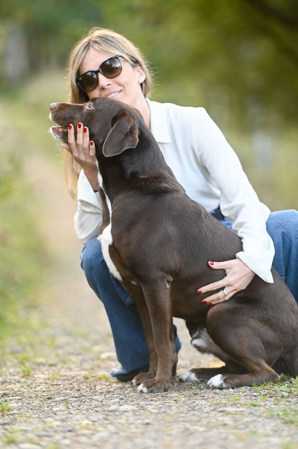 A chocolate Labrador puppy gives affectionate kisses while sitting outdoors with someone in casual attire.