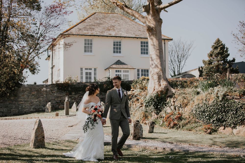 Bride and groom walk through a churchyard with a white Georgian manor house in the background.