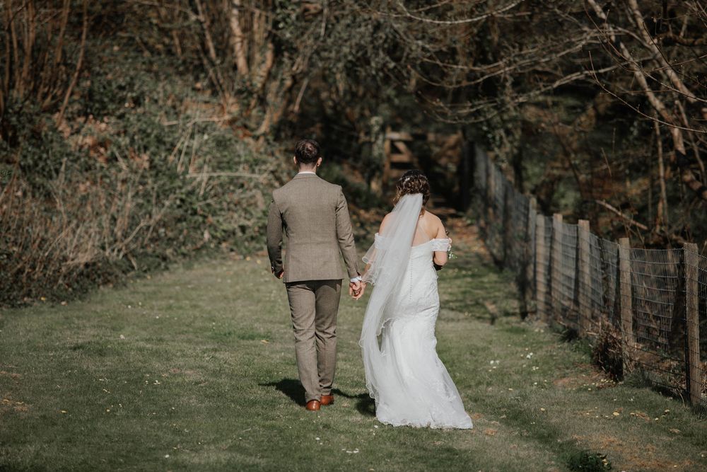 Bride and groom walking hand in hand through a lush green garden path on their wedding day.