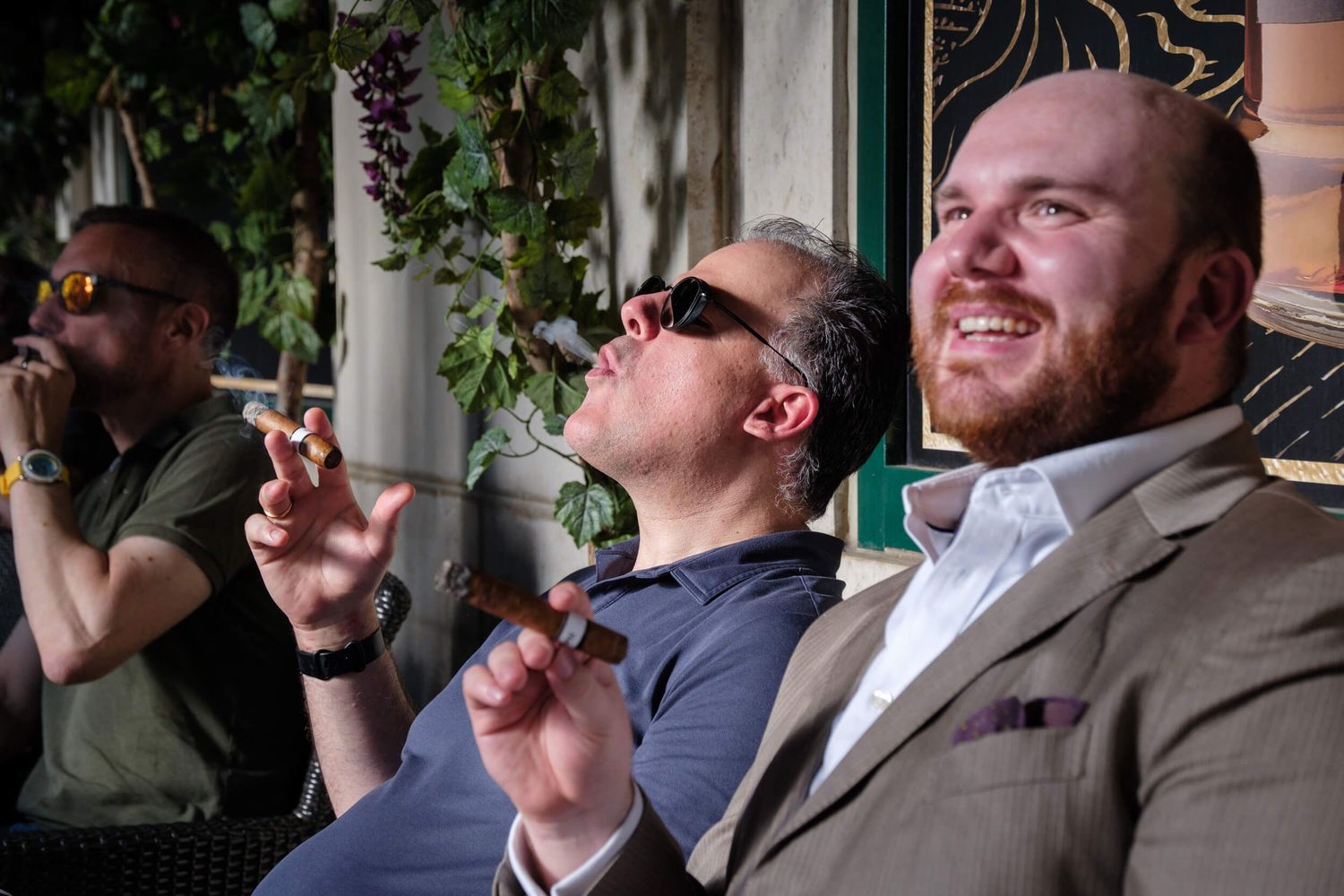 A group of people enjoying cigars and drinks together at an outdoor gathering.