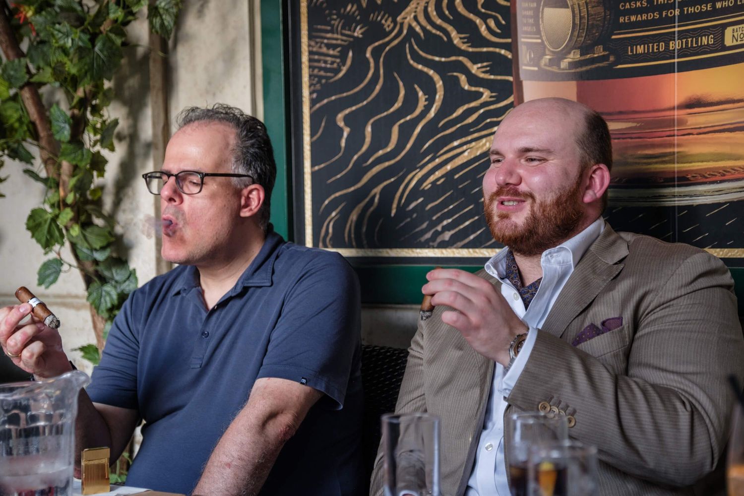 Group of people smoking cigars while seated at a table during an indoor social gathering.