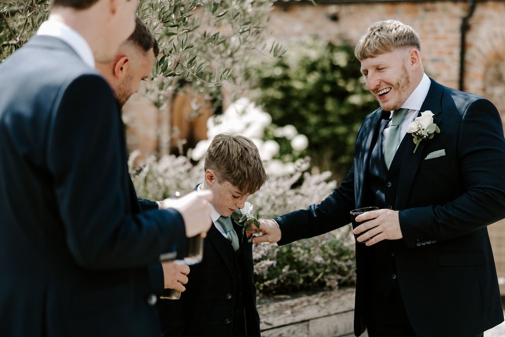 A candid moment between wedding party members in formal attire sharing laughter during an outdoor celebration.