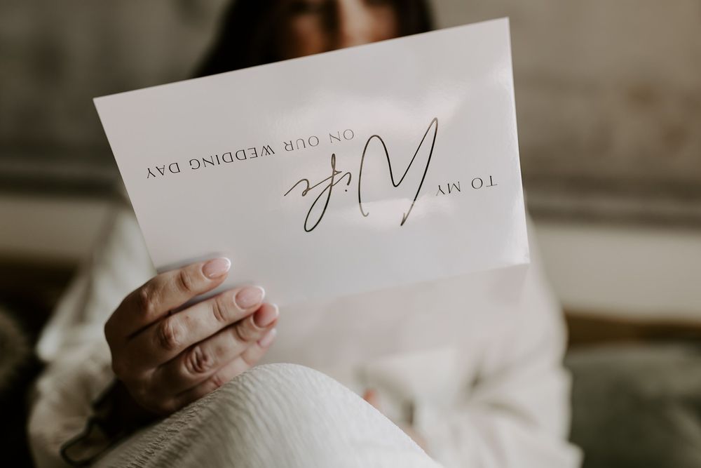 A person wearing a white sweater holds up a piece of paper in a well-lit interior setting.