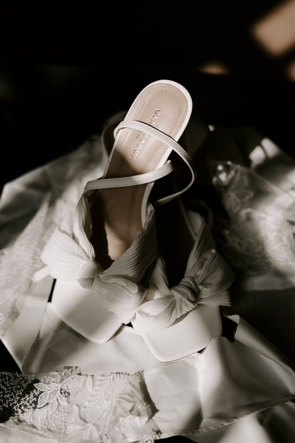 Elegant white bridal shoes arranged artistically with lace details in dramatic black and white lighting.