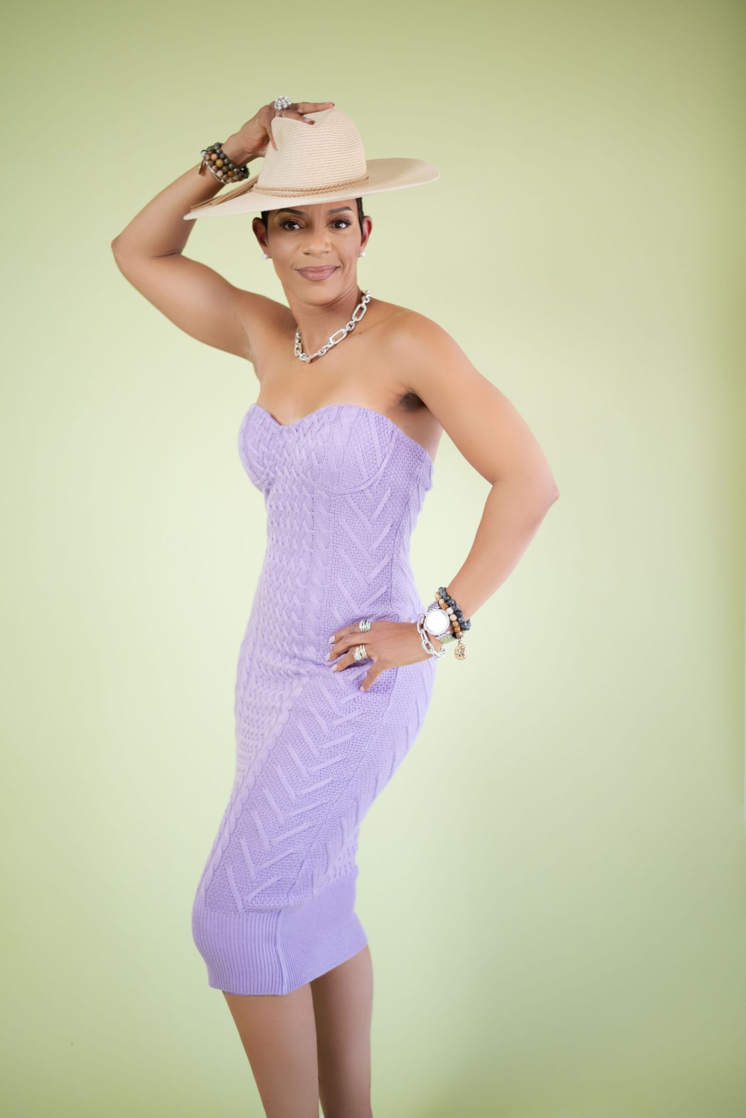 A person in a lavender romper strikes a playful pose against a light green background.