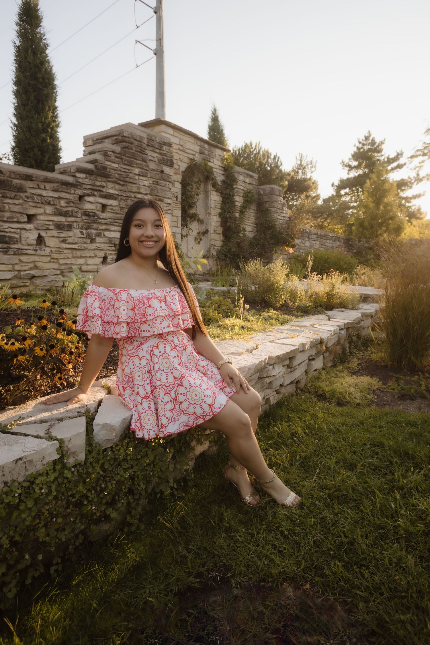 A child in a pink floral dress sits on stone steps in a garden during golden hour sunset.