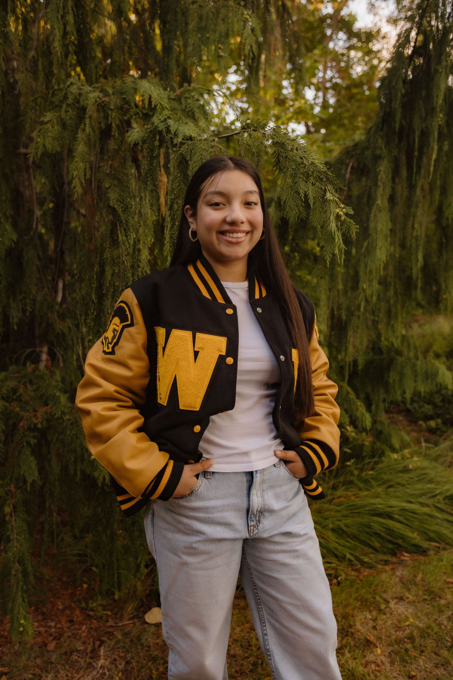 A letterman jacket and light jeans outfit shown in a series of cropped photos against a mossy forest backdrop.