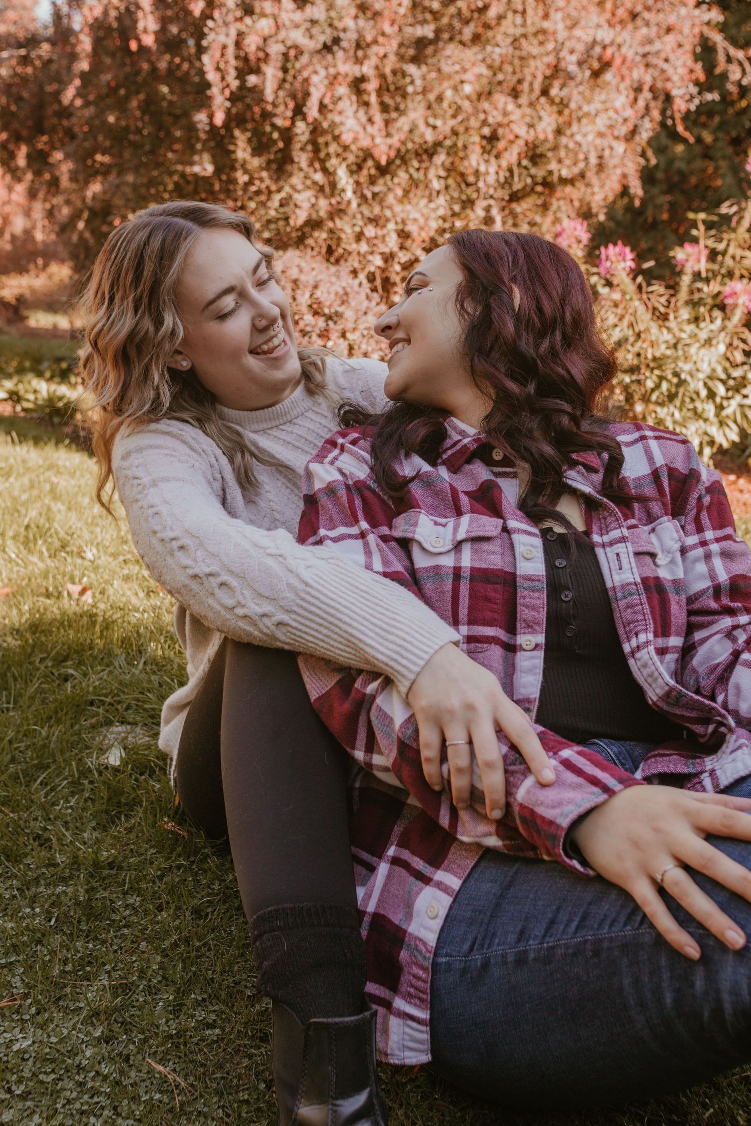 Couple in casual attire lying on grass during golden hour sharing playful and intimate moments in autumn setting.