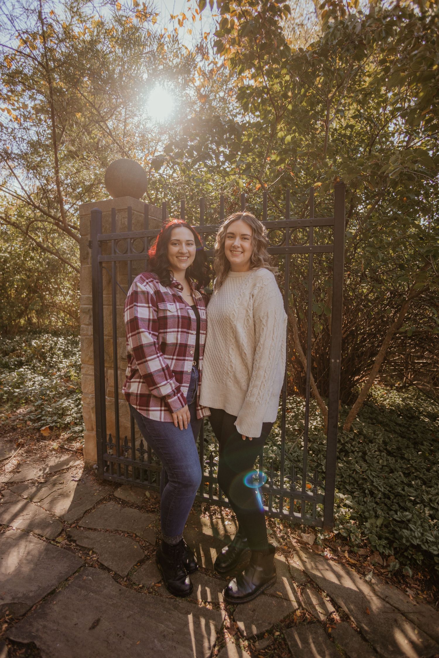 Two people stand together in front of a sunlit garden gate during golden hour.
