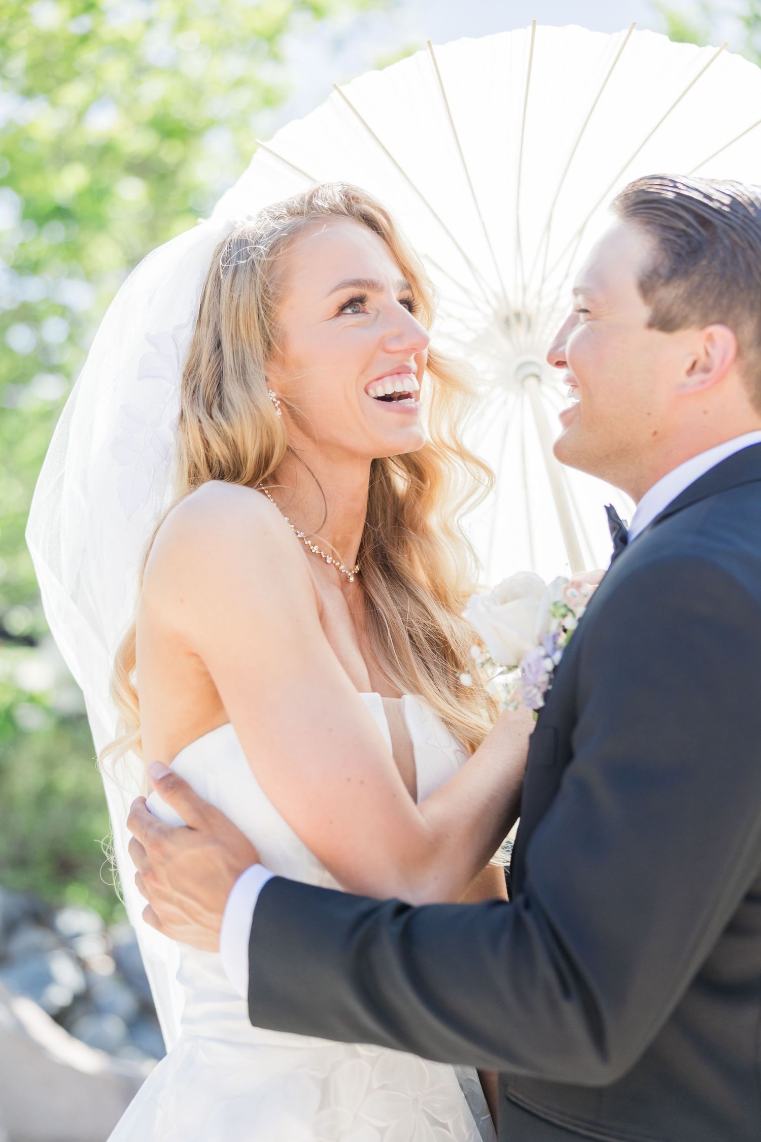 Romantic couple embraces against dramatic mountain backdrop with bride's veil flowing in the wind at sunset.