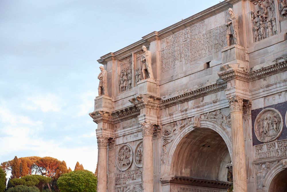 Ancient Arch of Constantine in Rome, Italy, featuring intricate carved reliefs and sculptures against a cloudy sky.