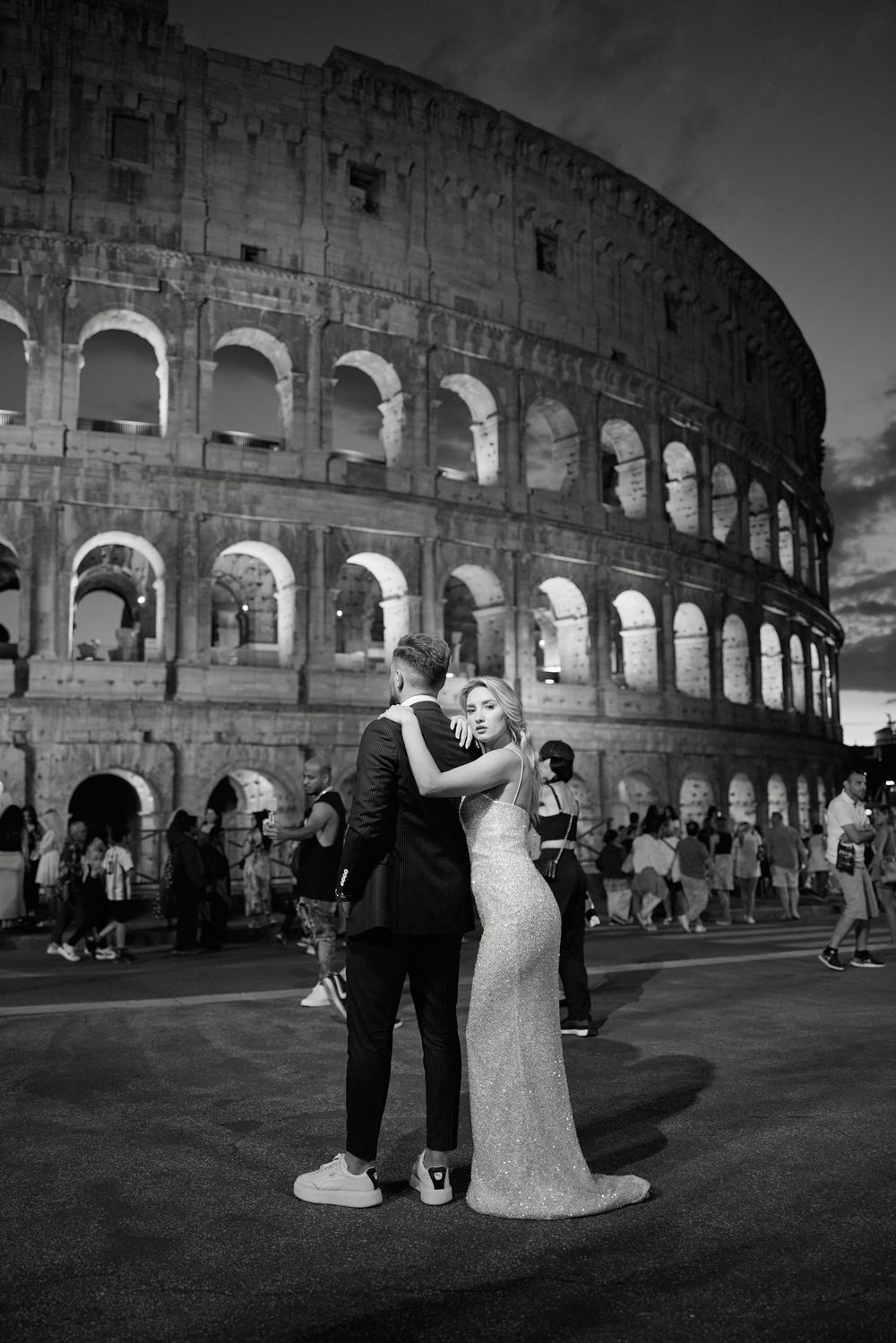 Bride and groom share a romantic embrace in front of the illuminated Colosseum in Rome at night.