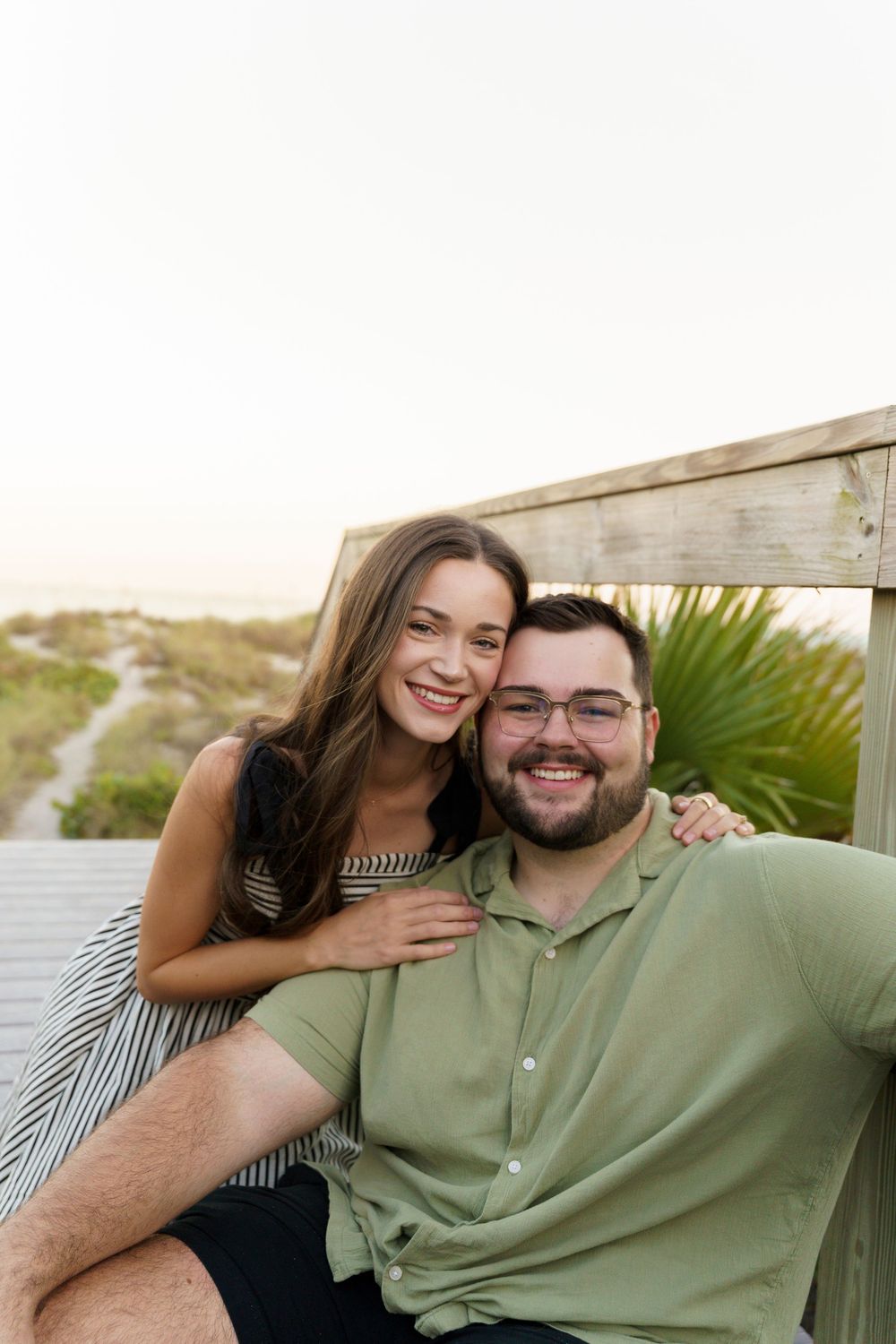 A couple shares a joyful moment together while sitting outdoors near tropical plants.