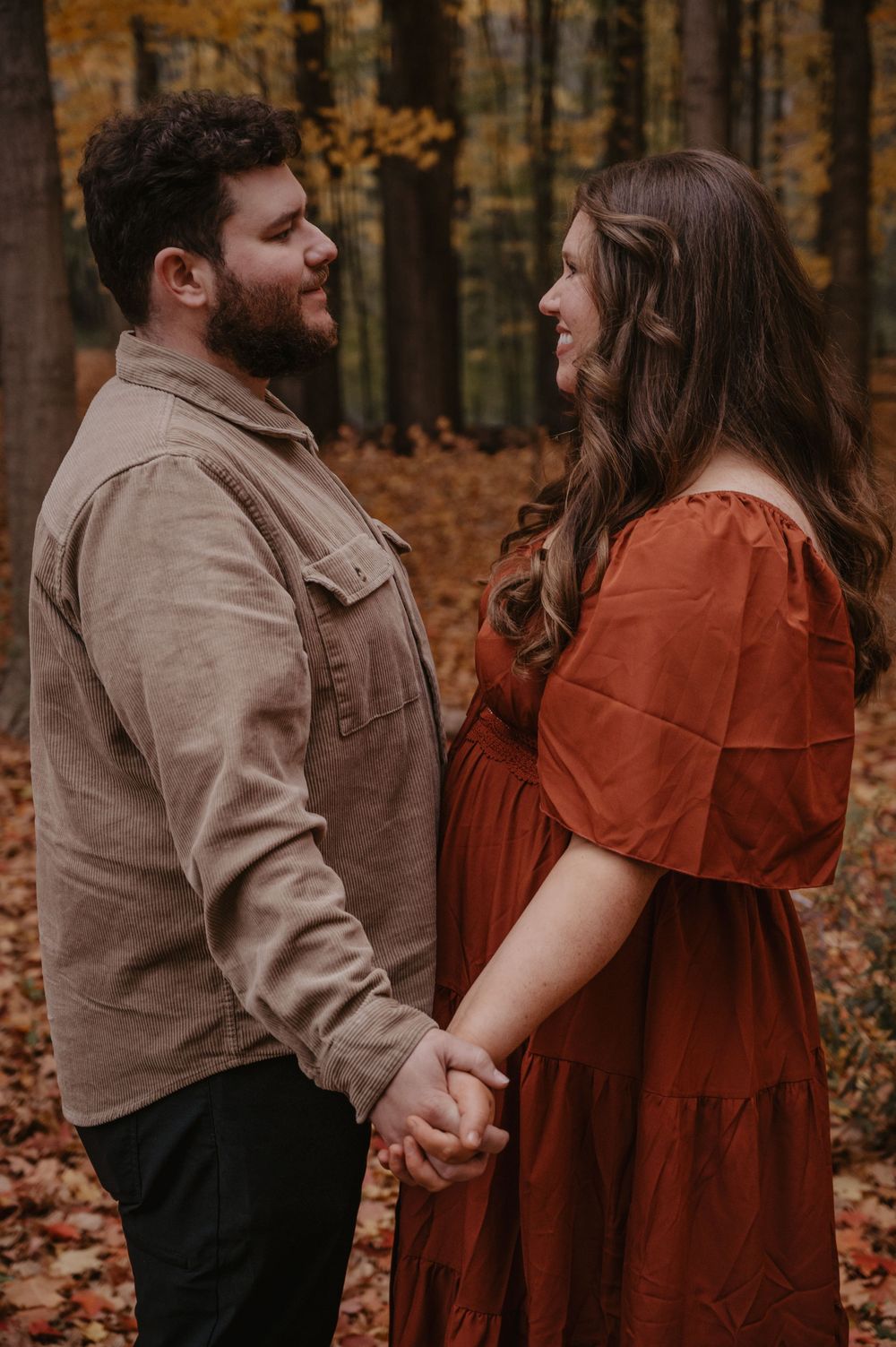 Couple holding hands and gazing at each other in golden autumn forest setting.