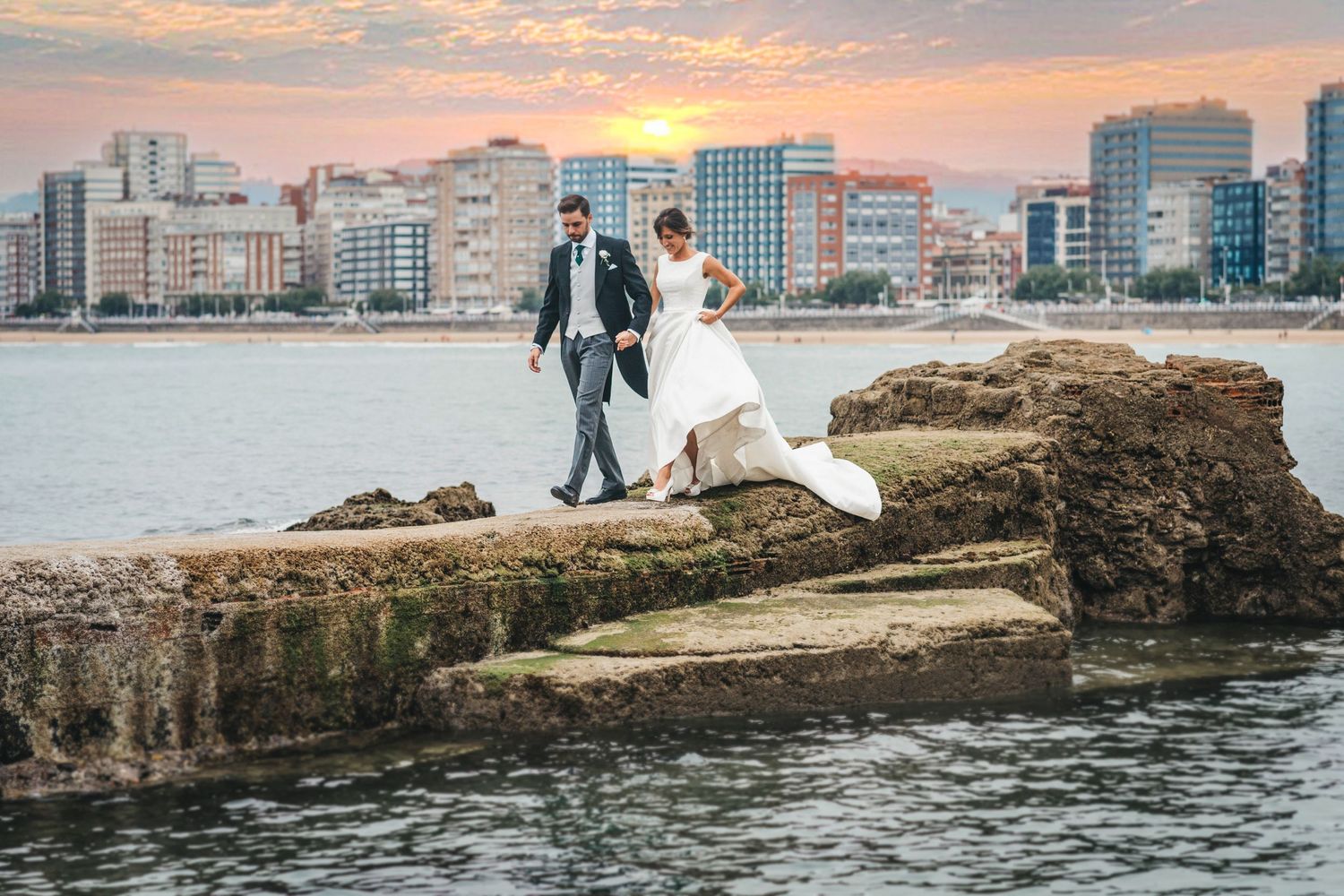 Fotografía documental de boda en Gijón. Novios pasean por el Club de Regatas de Gijón. La playa de San Lorenzo se ve al fondo.
