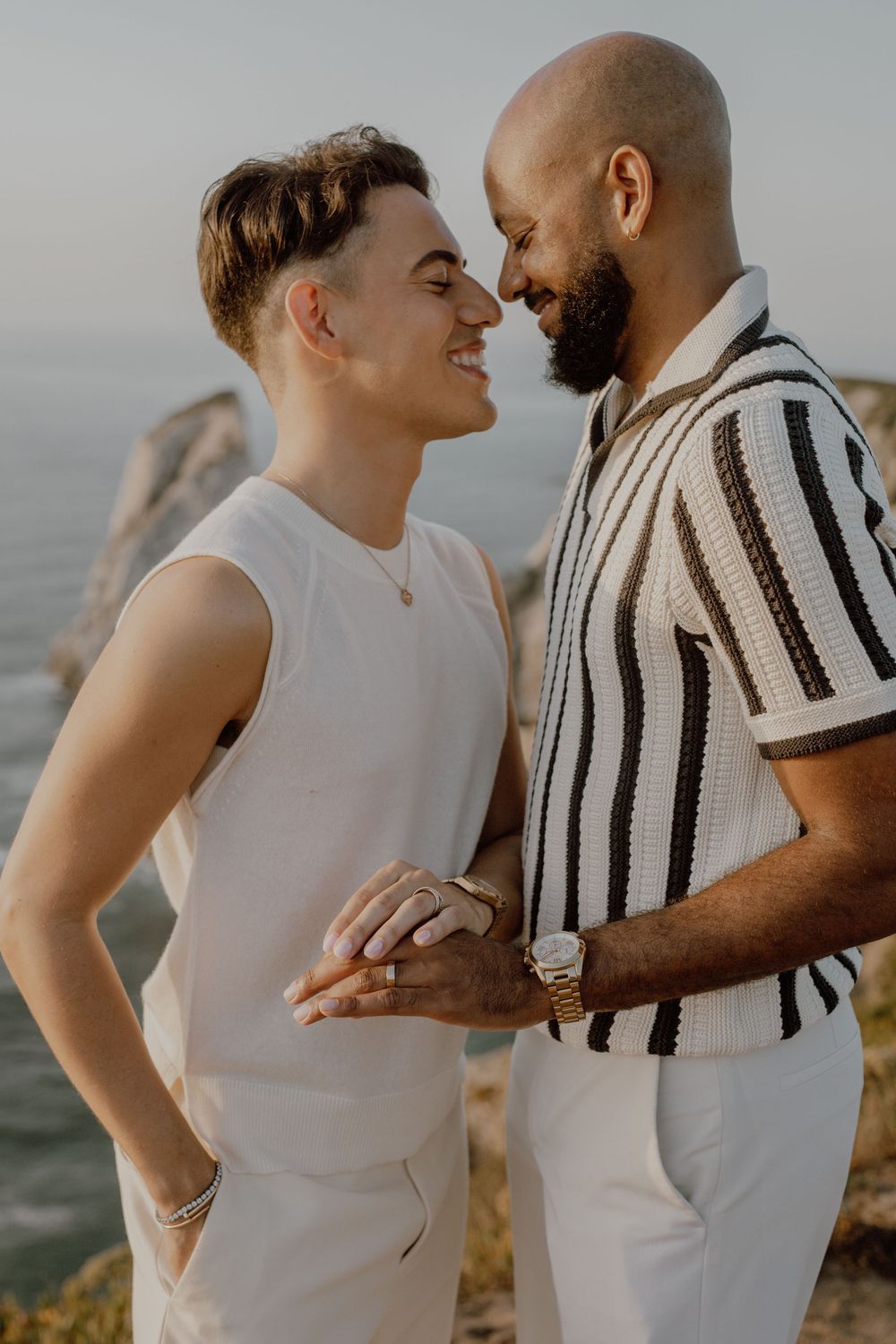 A couple in white and striped outfits share an intimate moment against a scenic outdoor backdrop.