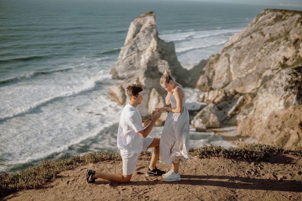 A romantic coastal wedding photoshoot with dramatic cliffs and ocean views at sunset.