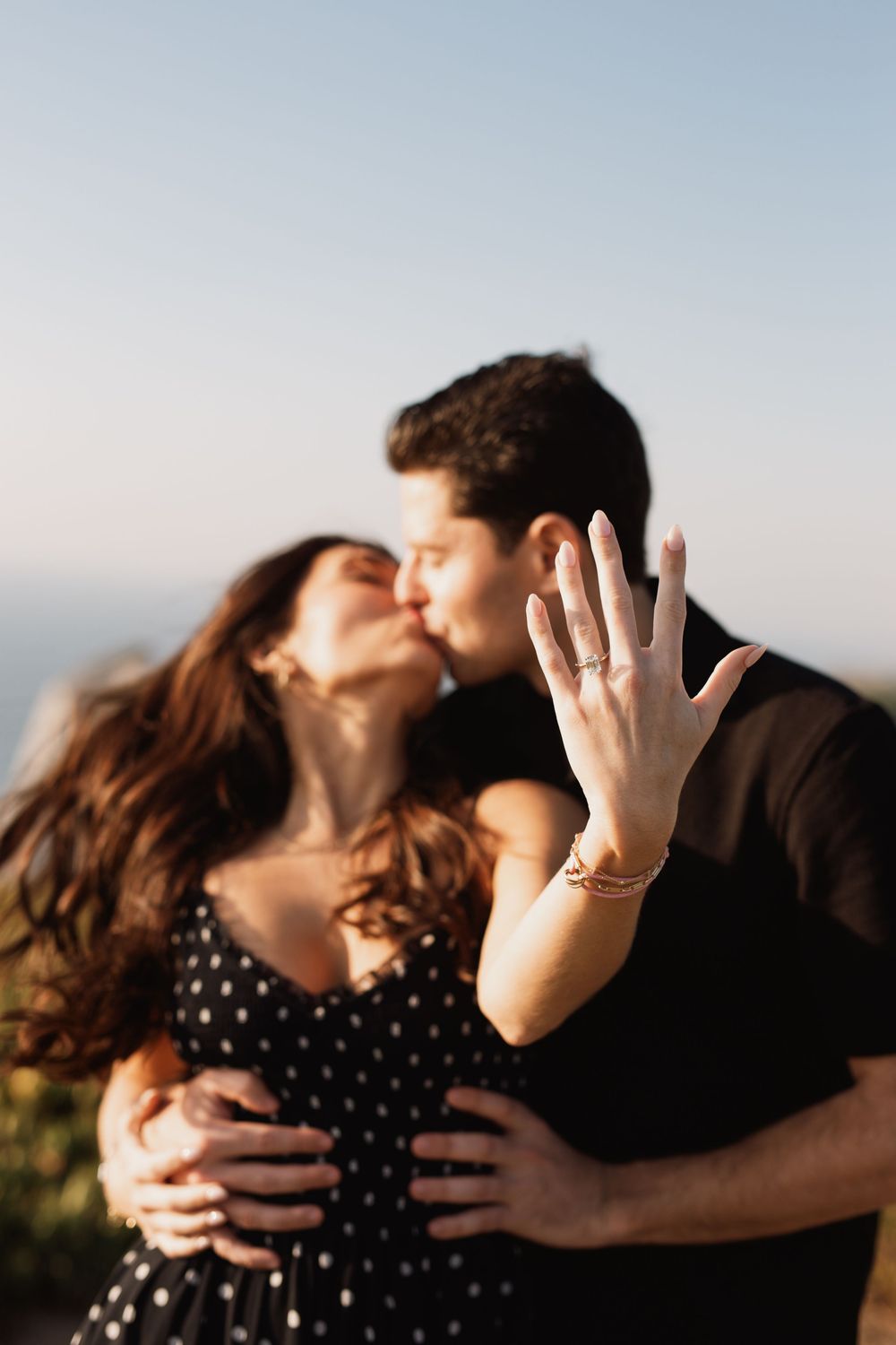 A romantic couple shares tender moments and displays their engagement rings against a scenic outdoor backdrop.