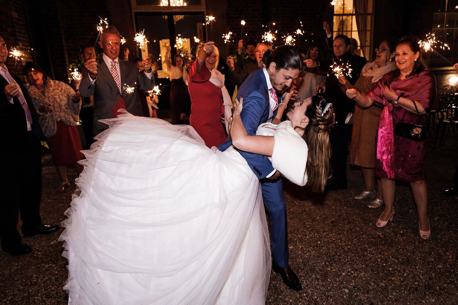 Bride and groom sharing an intimate embrace in the gardens at Hodsock Priory surrounded by guests with sparklers.