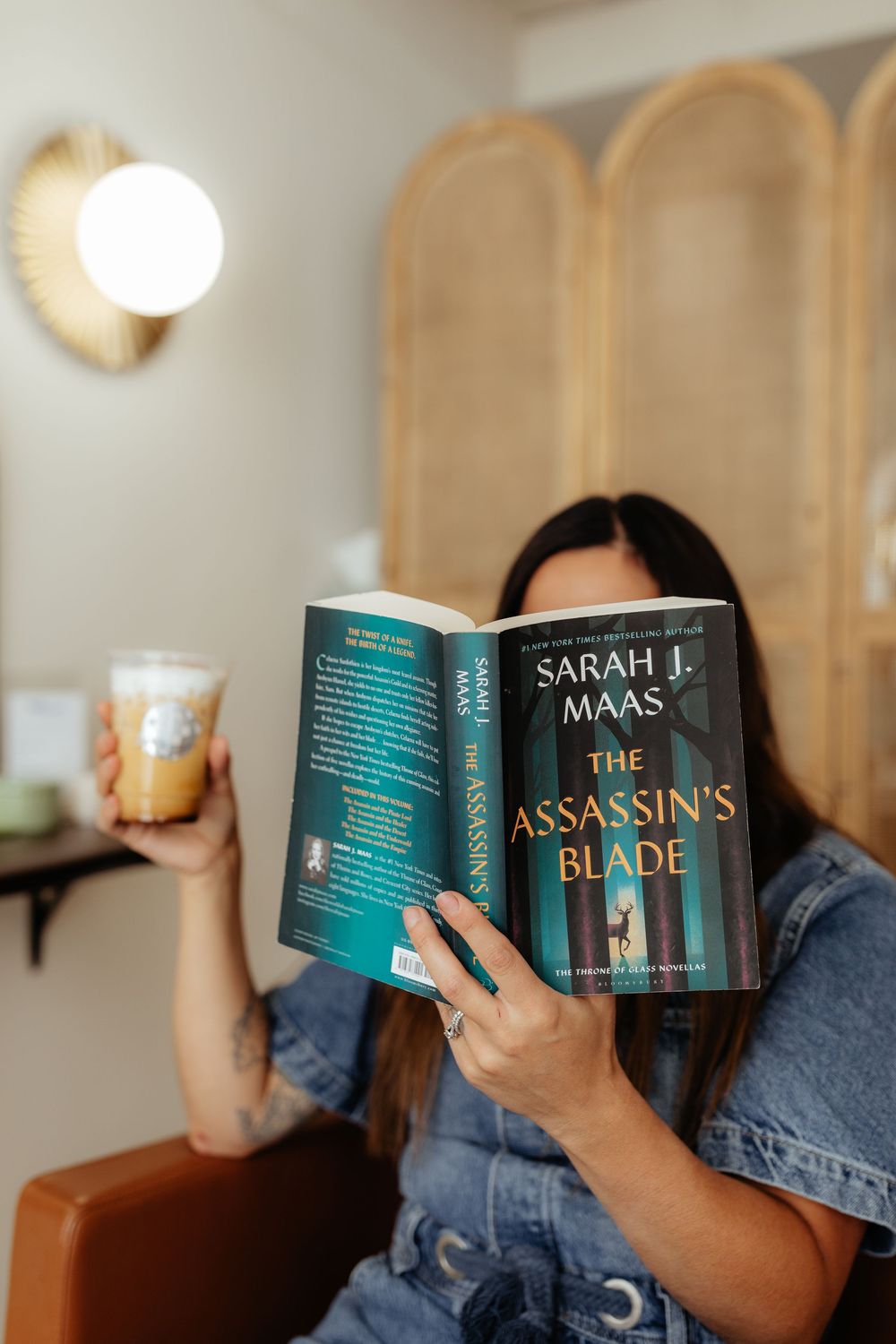 Person holding and reading 'The Assassin's Blade' book while sitting in a cozy room with warm lighting.