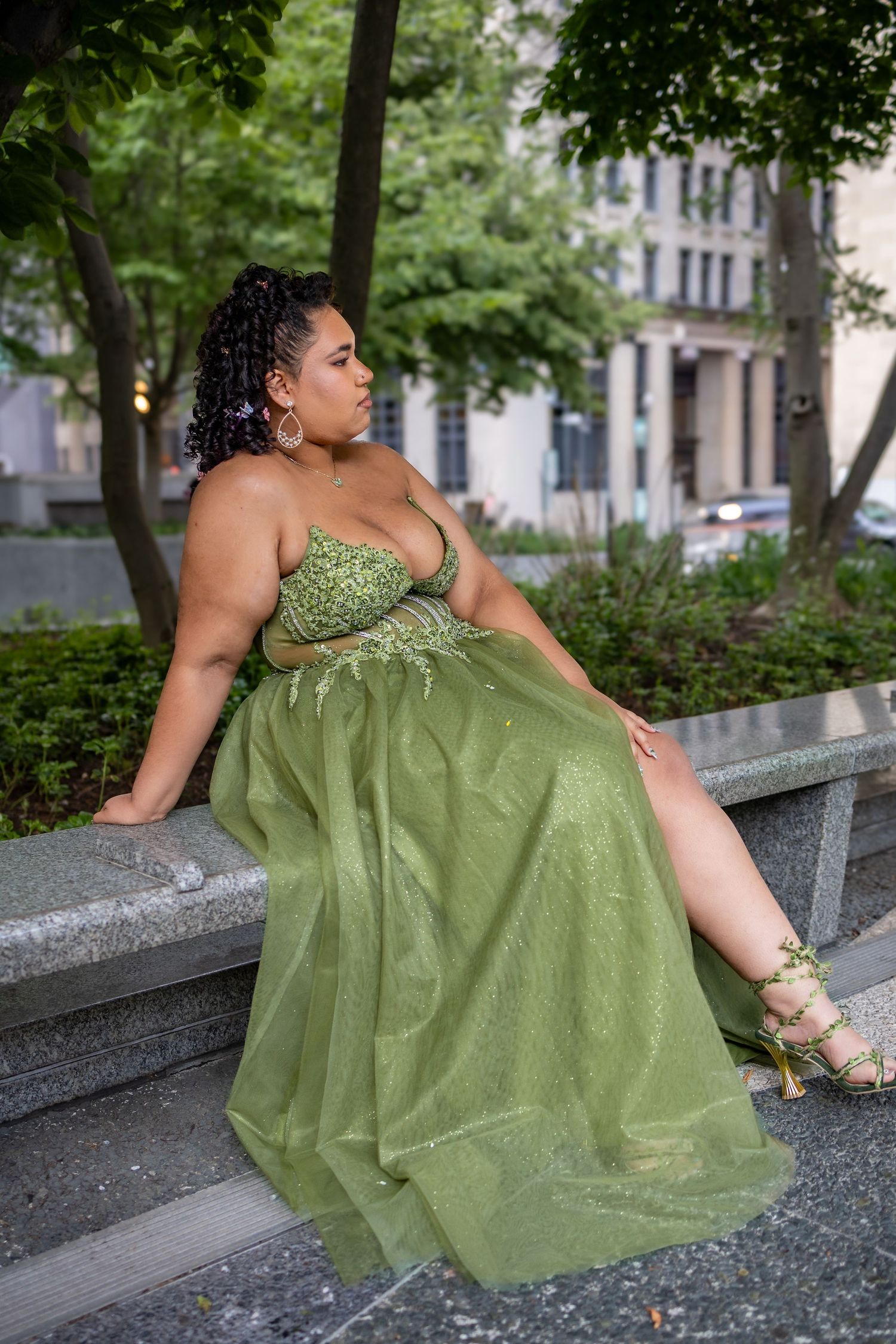 Woman in green beaded gown sitting on stone ledge outdoors.