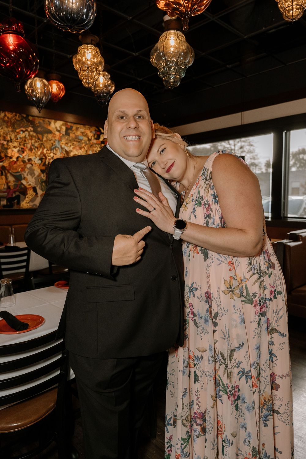 A couple shares a playful moment at a restaurant with warm lighting and decorative elements in the background.