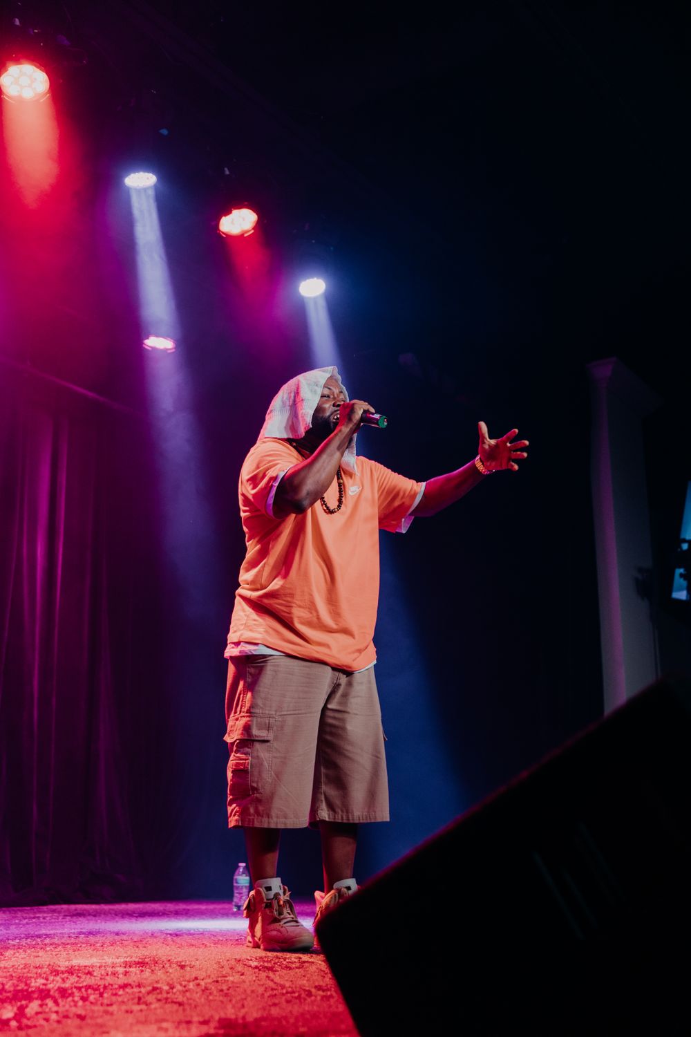 Performer in orange attire on stage with dramatic red and blue spotlights during a show.