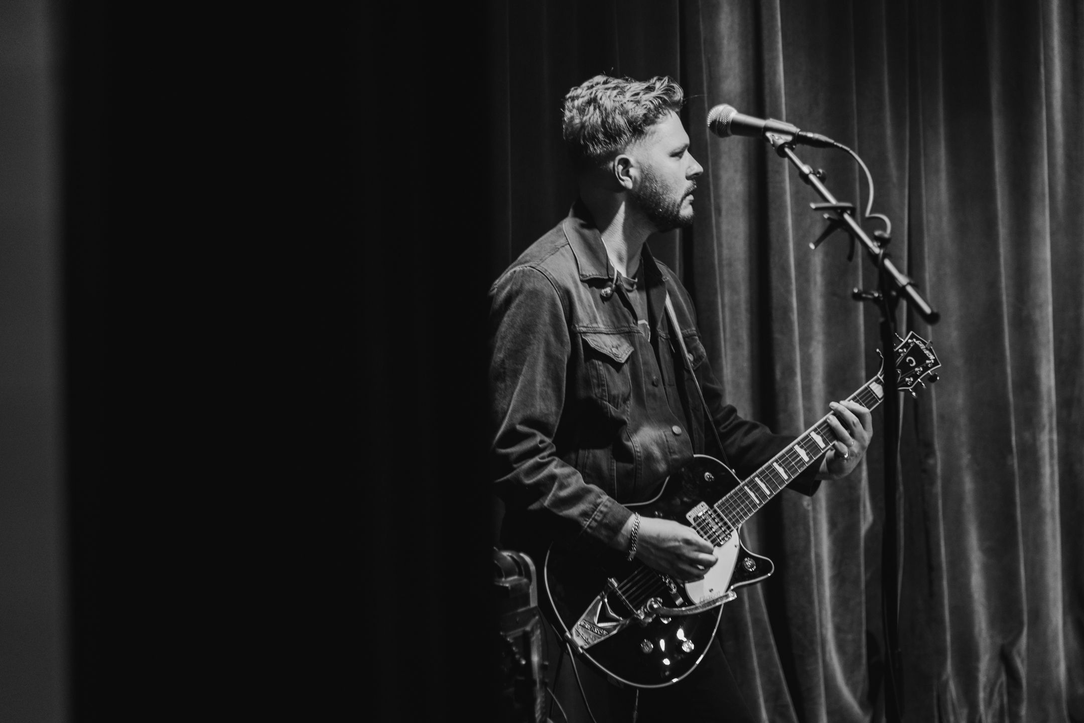 Black and white photo of musicians performing on stage with guitars and microphones.
