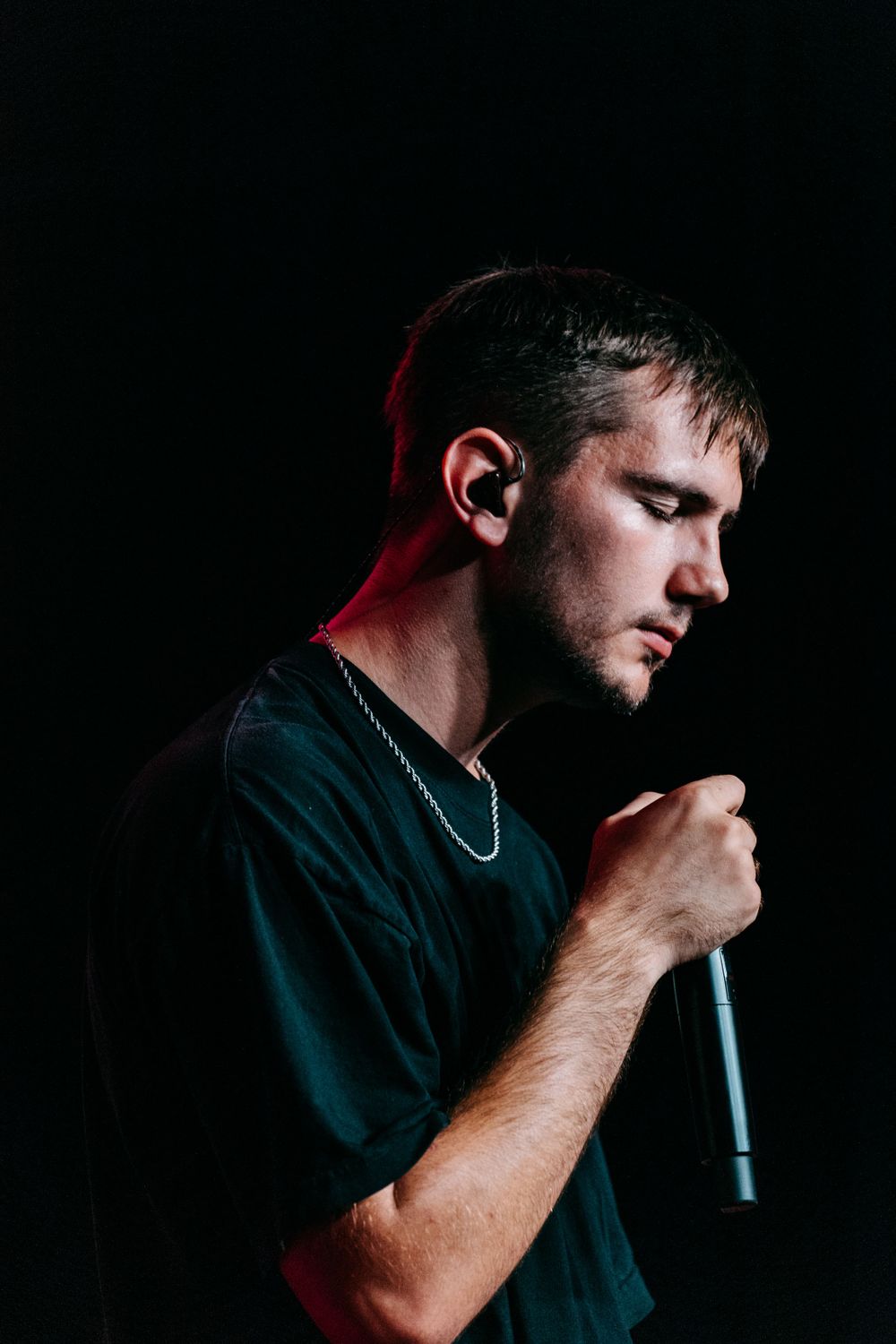 Dramatic side profile of a performer singing into a microphone in low-key lighting.