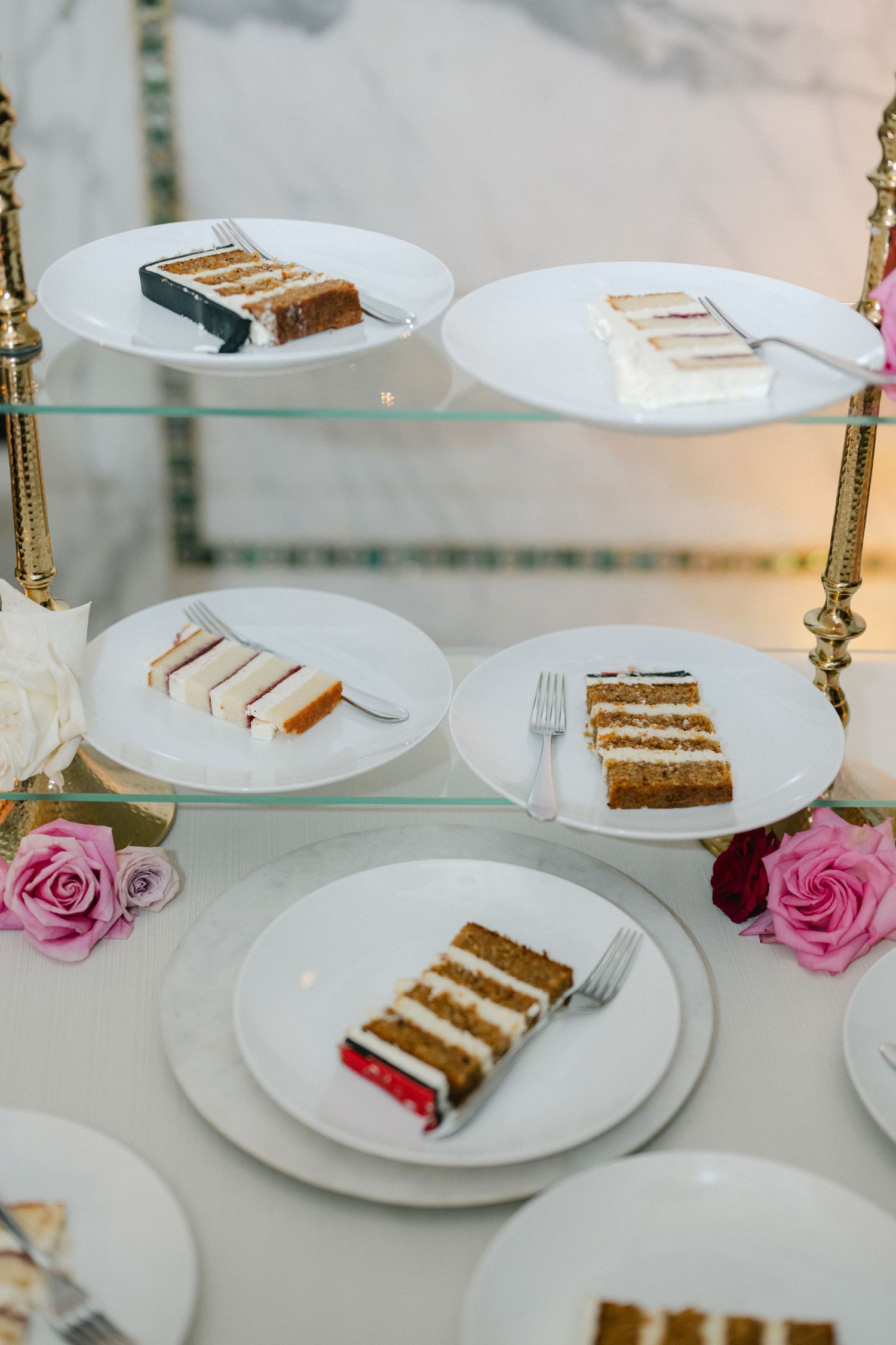 Layered carrot cake slices on white plates with pink roses as elegant table decorations.