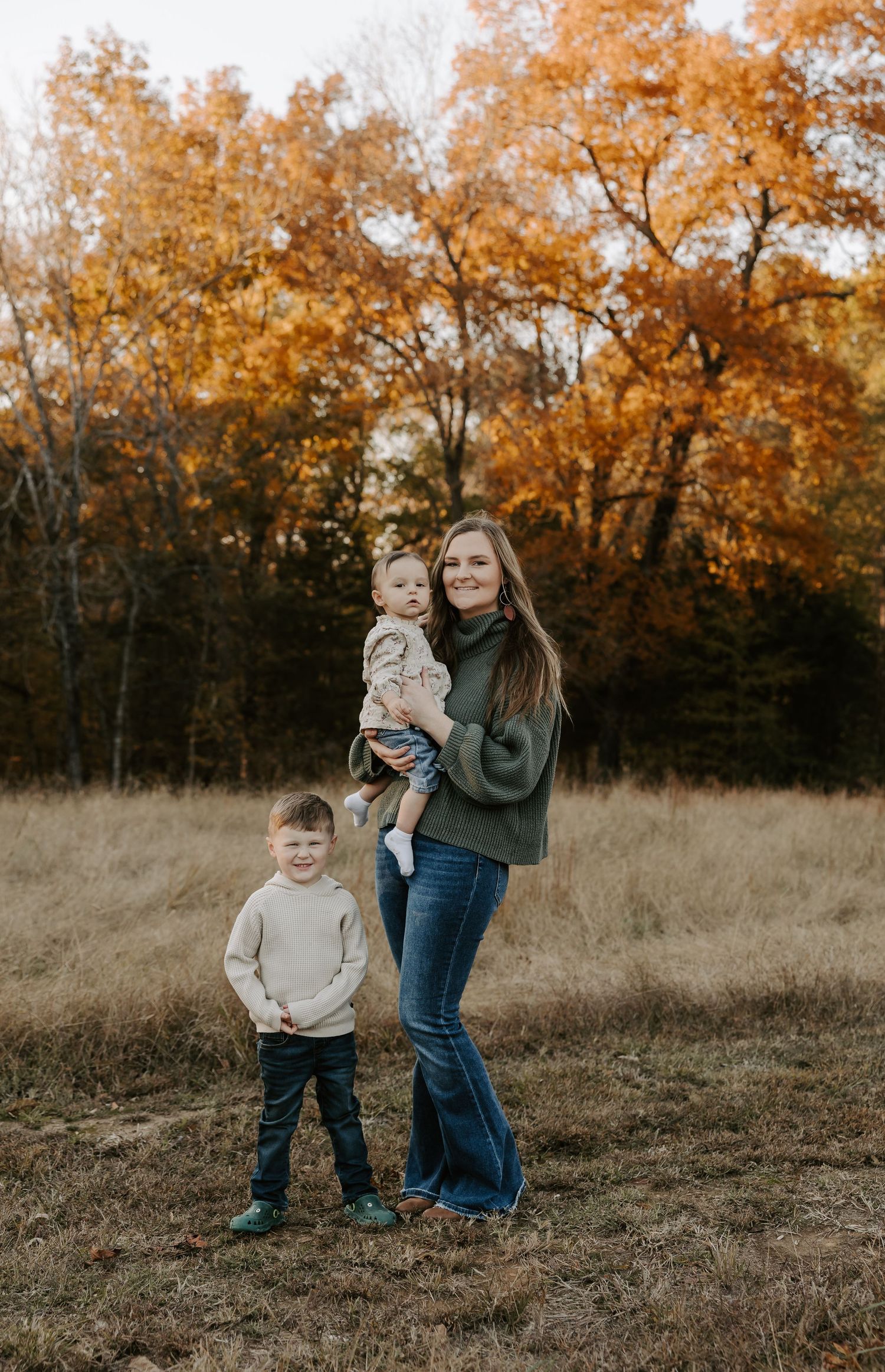 Family autumn portrait session in field with golden trees in background.