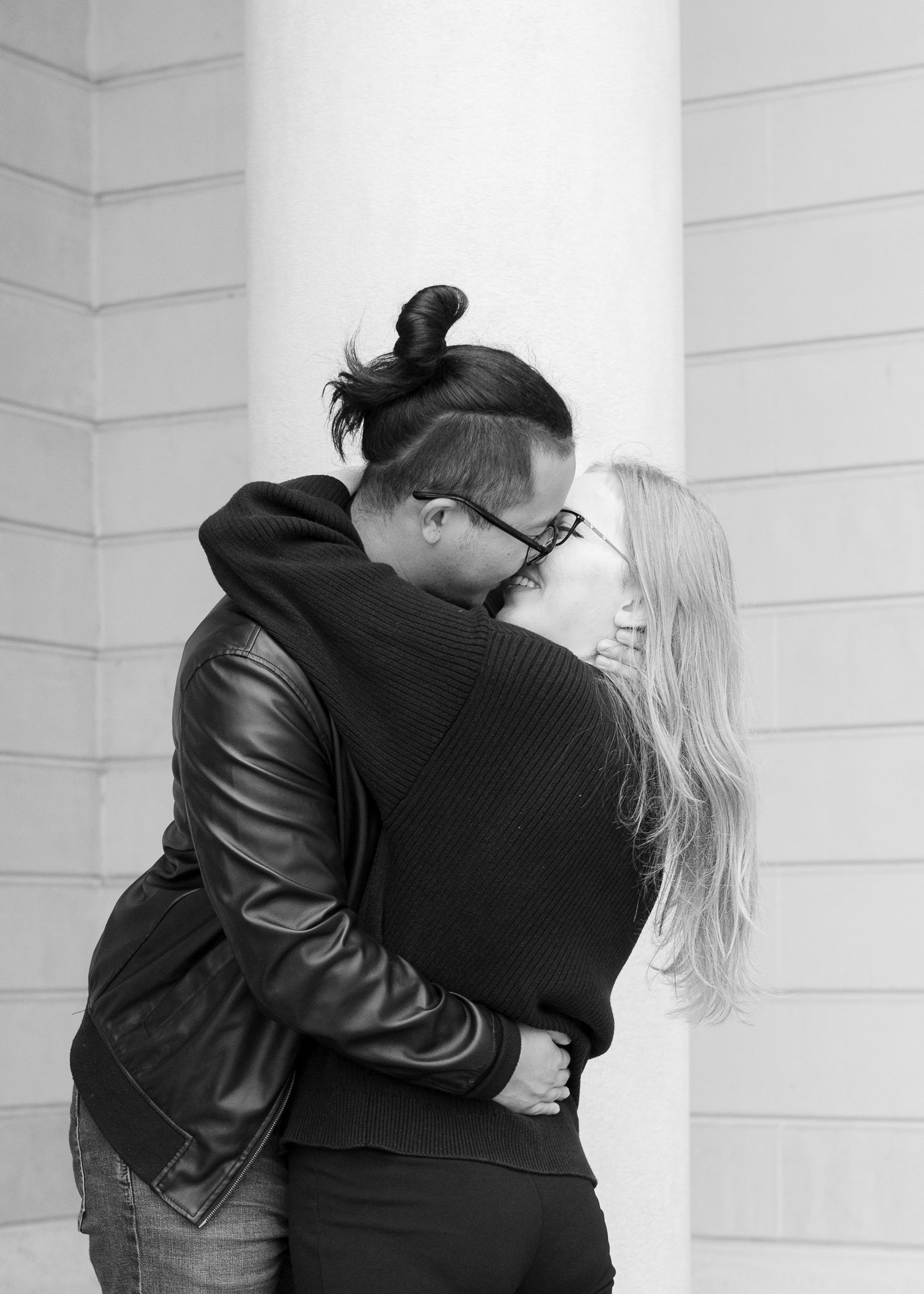 An intimate black and white portrait of a couple embracing against a white wall.