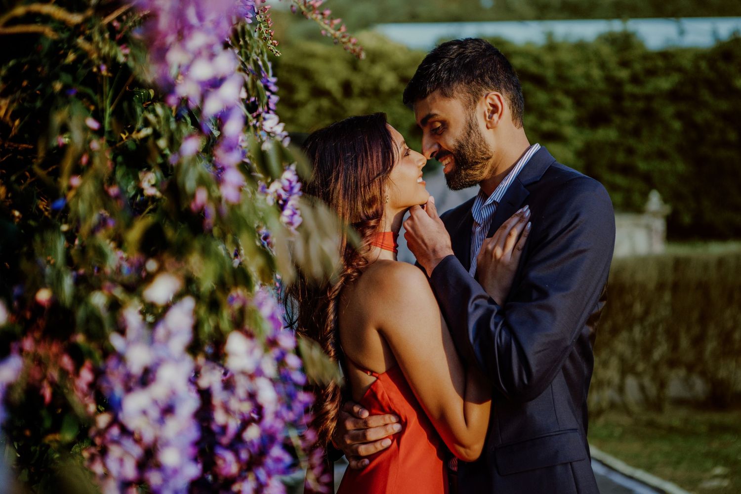 A tender romantic moment shared between a couple embracing near blooming purple wisteria flowers in a garden setting.